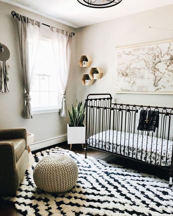 a black and white nursery with a printed rug, hexagon shelves and a map plus a neutral chair and footrest