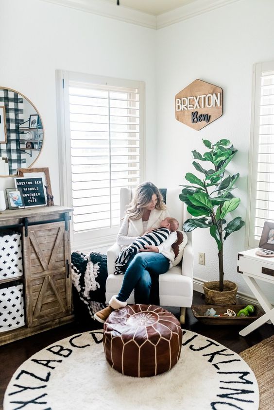 a boho farmhouse nursery with a leather ottoman, a printed rug, a reclaimed wood dresser and a potted plant