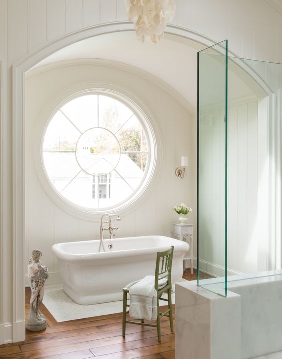 a chic and neutral bathroom is made catchier and more interesting with a porthole window over the bathtub