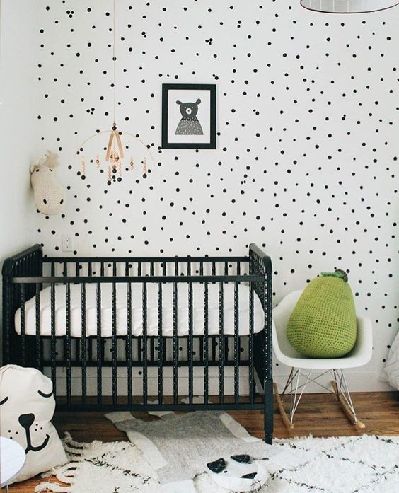 a chic black and white nursery with a black crib, a spotted wall, a printed rug and a single green pear pillow for a touch of color