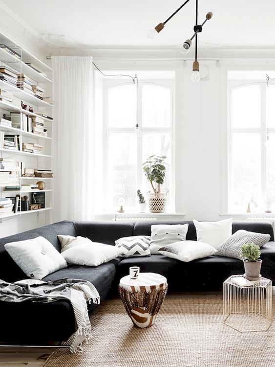 a chic living room with shelves, a black sectional, a couple of catchy coffee tables and a jute rug