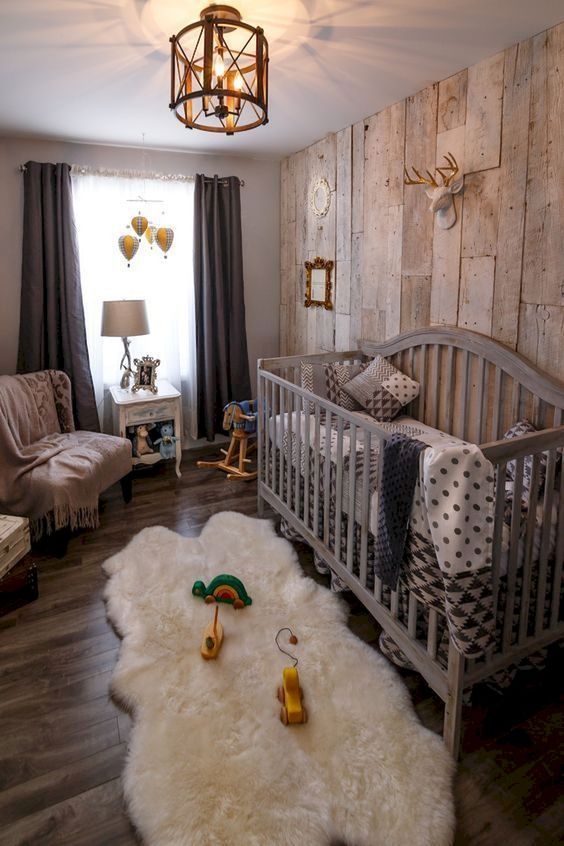 a cool rustic nursery with a reclaimed wood wall, a large grey crib, a fluffy rug, dark curtains and a vintage chandelier