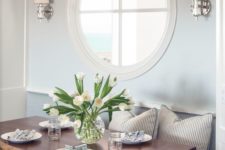 a cozy dining nook with a porthole window and wall lamps looks very refined and very chic