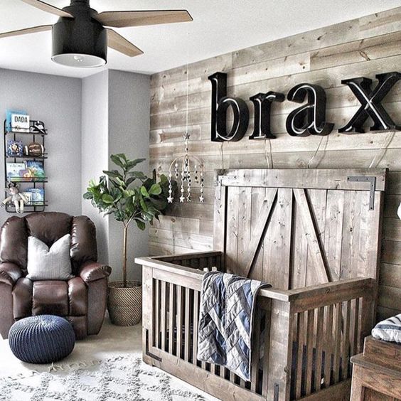 a cozy farmhouse nursery, a reclaimed wood wall and a matching crib, a name on the wall, a leather chair and a lamp fan