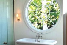 a modern farmhouse with a large porthole window next to the tub to fill the space with natural light
