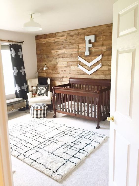 a rustic nursery with a printed rug, a stained crib, a reclaimed wall and some touches of prints