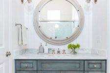 a shabby chic coastal bathroom with an ged wood vanity and a large porthole window to the shower