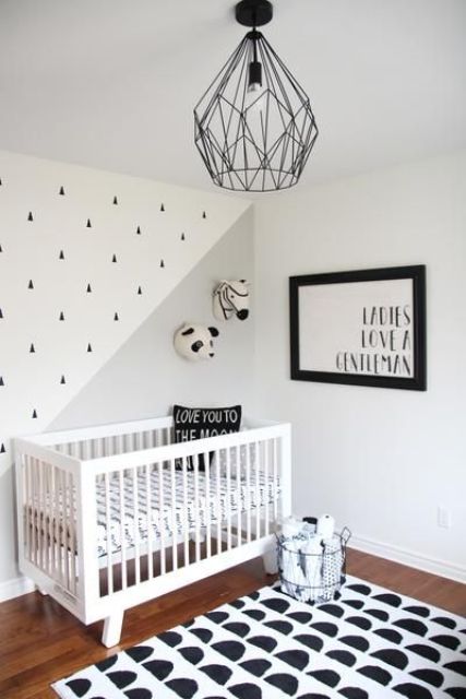 a simple contemporary nursery with a printed rug and wall, a grpahic artwork and a geometric black lamp