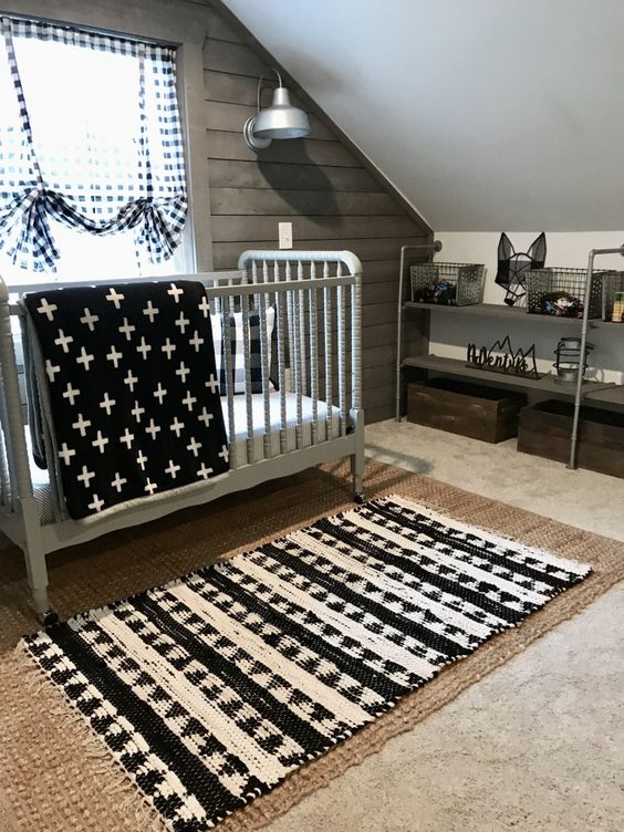 a small attic nursery with a jute rug, a printed one, a grey vintage crib, prints and a reclaimed wooden wall