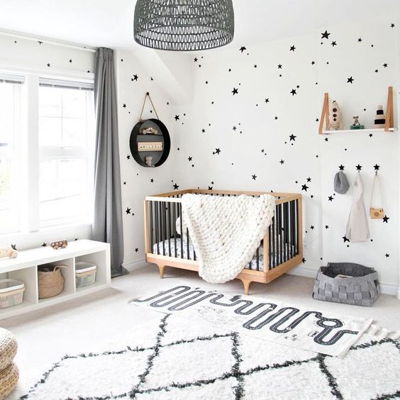a stylish black and white space with a printed rug, star print walls, a contemporary crib and a black lampshade