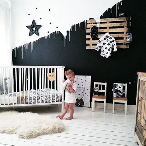 a stylish black and white space with an accent wall, a pallet clothes rack, a white crib and some more monochromatic touches