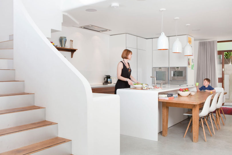The kitchen is done with sleek white cabinets, catchy pendant lamps and some wooden furniture
