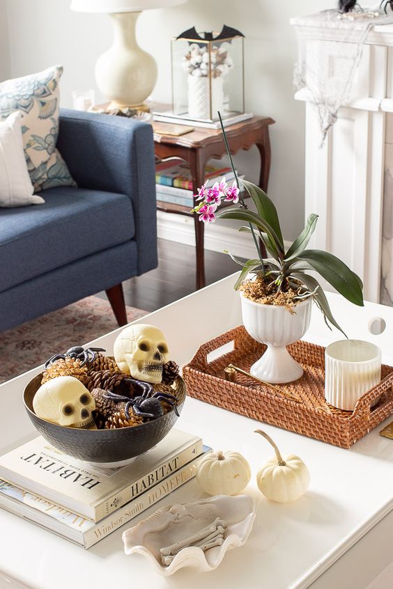a chic Halloween coffee table with a potted bloom, a bowl with spiders, skulls and pinecones and some bones in a shell