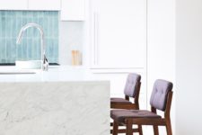 The kitchen is done with white cabinets, a white marble kitchen island and tall stools that contrast the whole space