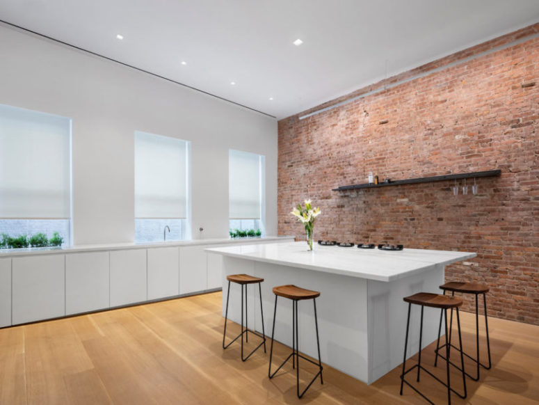 The kitchen is white and long, there are no upper cabinets and a white kitchen island with stools for eating