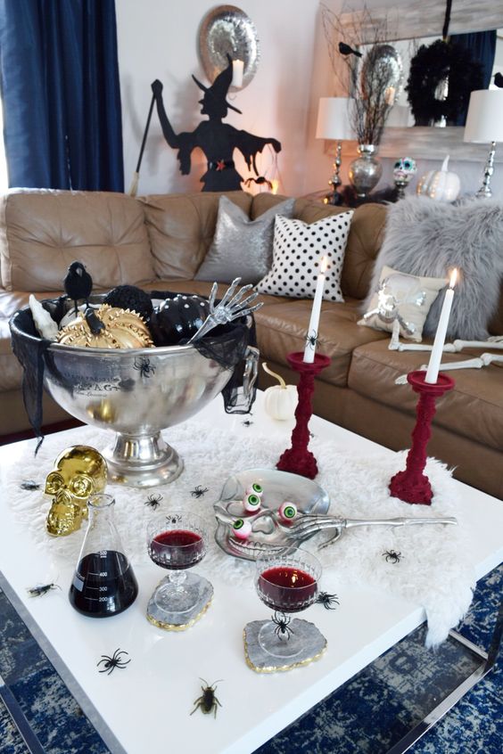 a Halloween coffee table with burgundy candleholders, skulls, fake eyes and metallich arms, black and gold pumpkins in a large bowl