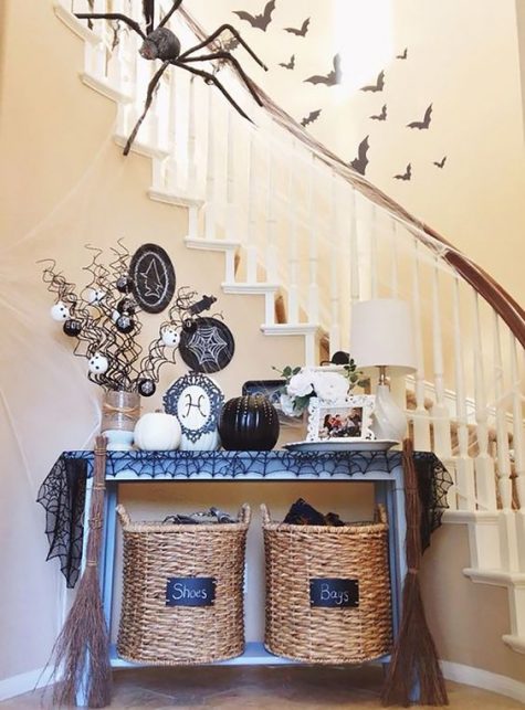 a console covered with a black spiderweb tablecloth, black and white pumpkins, ornaments and plates