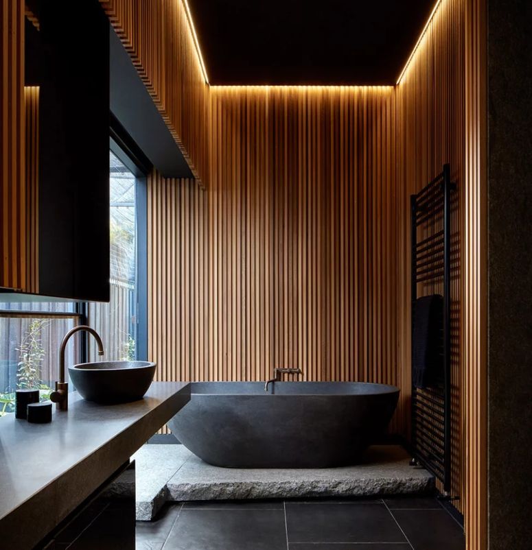 The wonderful moody bathroom is done with a stone tub on a platform, built in lights over it, a stone vanity and some minimalist textures The wonderful moody bathroom is done with a stone tub on a platform, built-in lights over it, a stone vanity and some minimalist textures