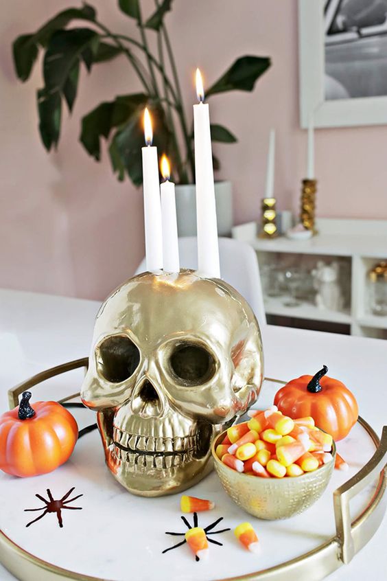 a simple Halloween arrangement of a tray with candy corns, faux pumpkins, spiders and a gold skull as a candleholders