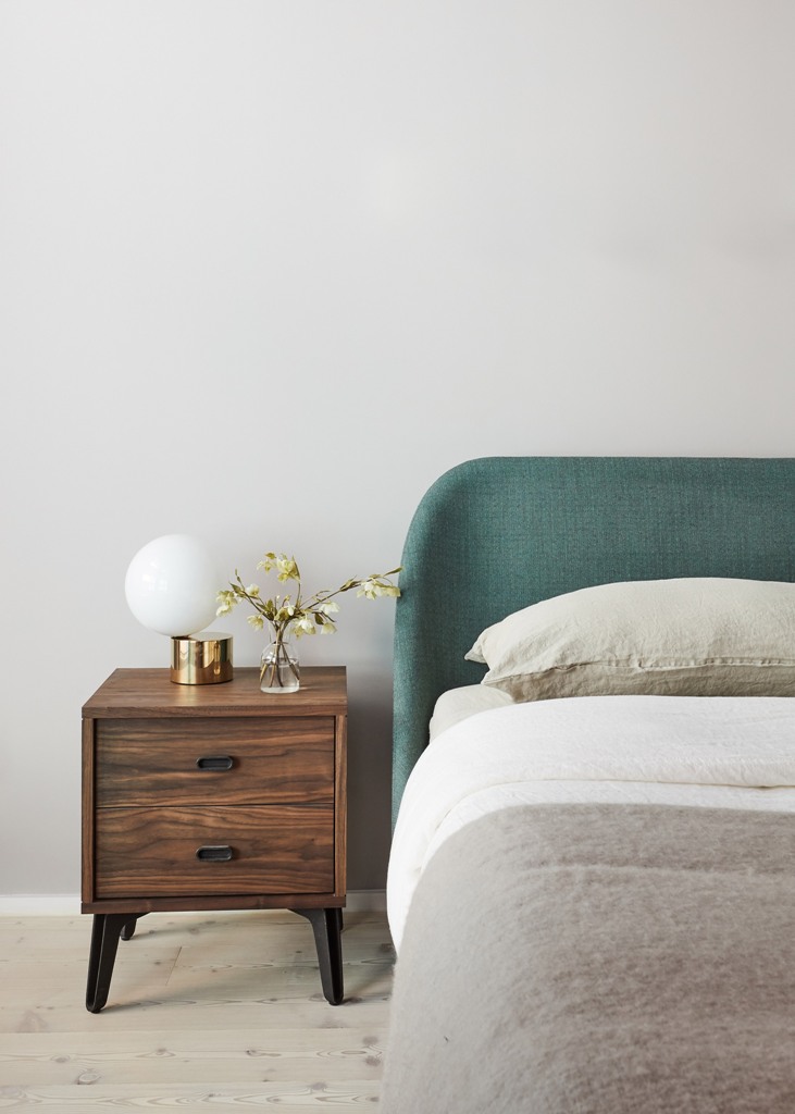 The bedroom is done with an upholstered bed, a rich stined nightstand, some neutral textiles and metallic touches