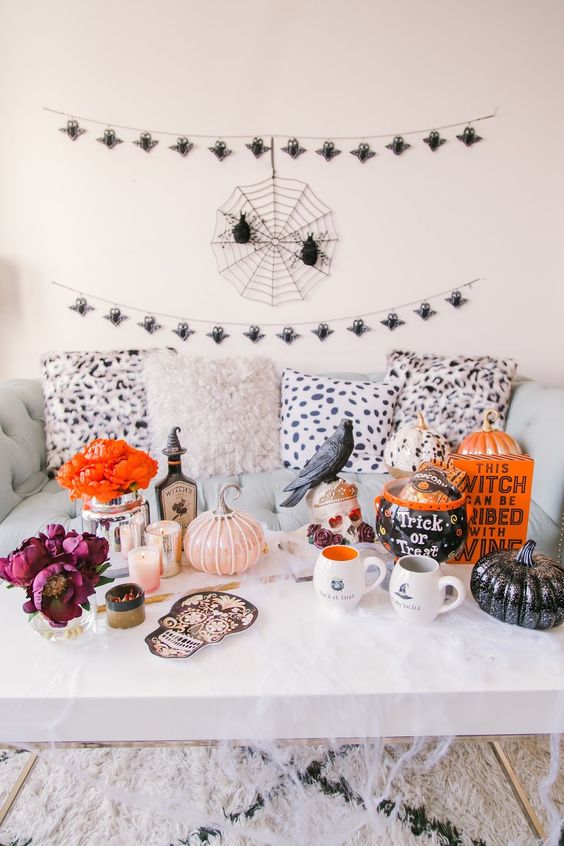 a whimsy coffee table with faux pumpkins, blackbirds, candles, a sugar skull, some witch potion and a book plus bold blooms