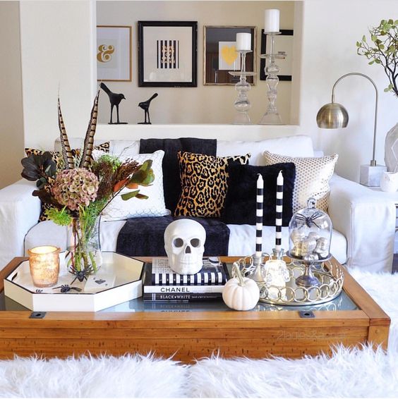 Halloween coffee table decor with a skull, skulls in a cloche, pumpkins, dried blooms and feathers plus candles