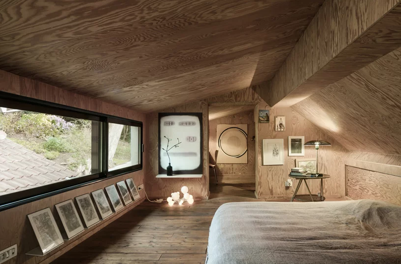 The master bedroom is designed like a cabin and is all clad with light colored plywood, there some lights, art and a work space