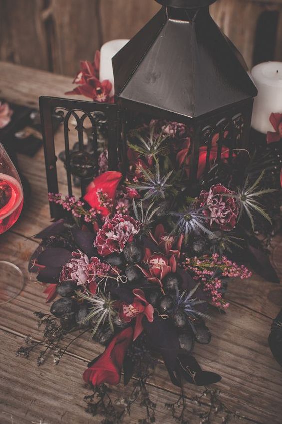 a gorgeous and sultry Halloween centerpiece of a black lantern, fuchsia and red blooms, thistles and grapes