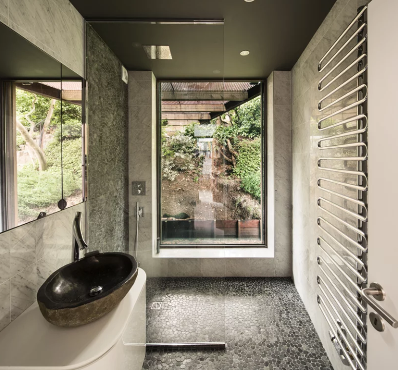 The bathroom opens towards nature and is decorated with pebbles and marble tiles