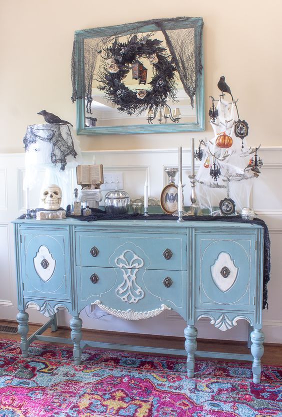 a refined Halloween console with an antler Halloween tree with black and orange ornaments, skulls, blackbirds and a dramatic black wreath