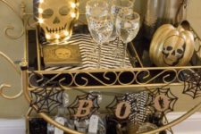 16 a gorgeous black and gold Halloween bar cart with skeletons, striped mats, a garland with spiderwebs and a hand candleholder