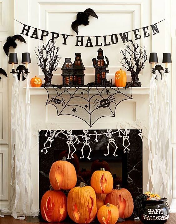 a bright Halloween mantel with carved pumpkins, skeletons, a piderweb, haunted houses and a banner over it
