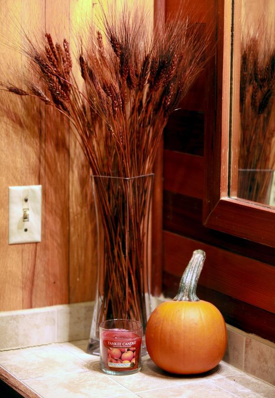 a fall scented candle, a pumpkin and a wheat arrangement make the bathroom feel rustic and fall like