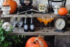 18 a Halloween drink bar with a pumpkin, skulls, blackbirds, spiderweb, greenery and skeleton hands