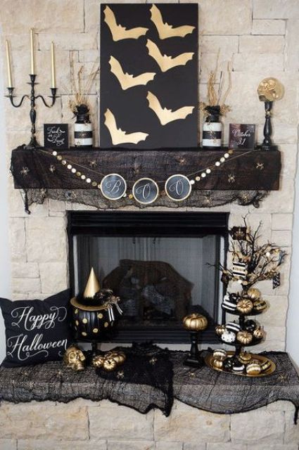 a stylish black and gold Halloween mantel with bats, candles, vases with branches, skulls and lots of painted pumpkins is wow