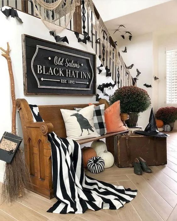 a gorgeous Halloween entryway with large pumpkins, black and white fabric, a witch broom, hat, shoes and some bats