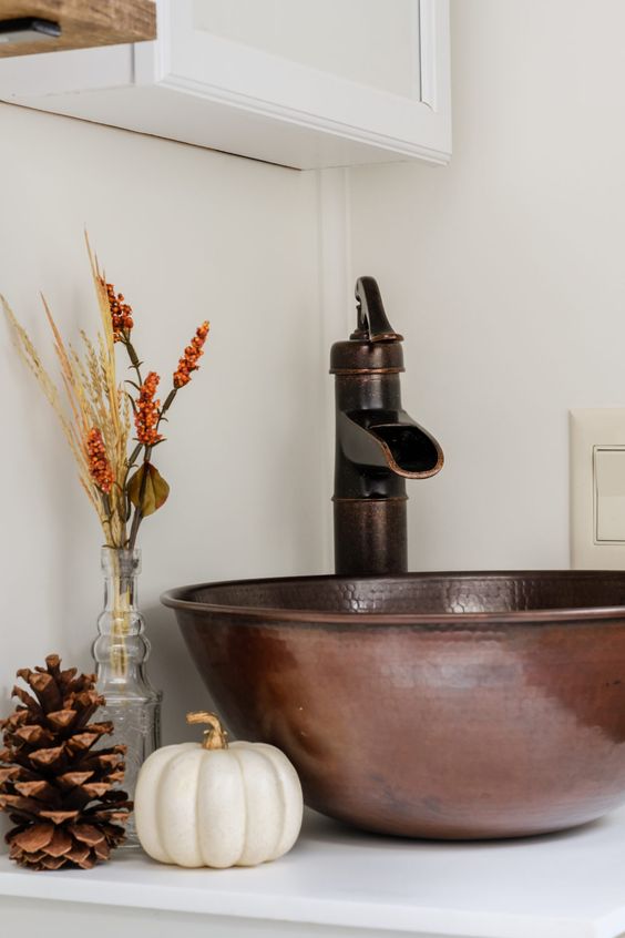 a hammered copper sink and faucet, a pumpkin, pinecone and a dried arrangement for pretty fall bathroom decor