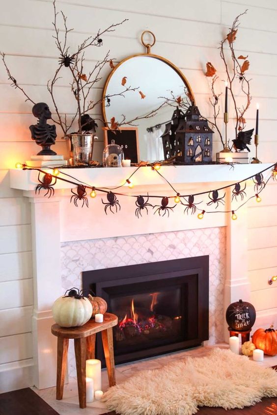 a scary Halloween mantel with natural pumpkins, a spider bunting, lights, a house, some busts and branches with leaves