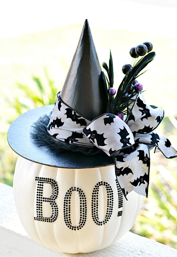 a creative centerpiece of a white pumpkin with letters, a witch hat with a bow and feathers for Halloween