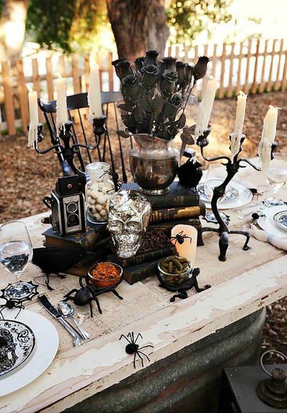a whimsy centerpiece of stacks of books, a silver skull, candles, a vintage camera, a vintage silver vase with black roses