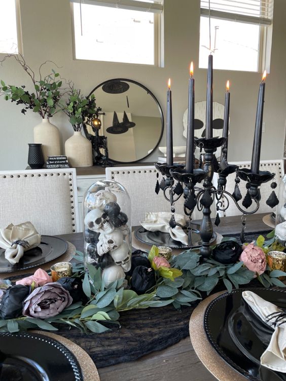 a Halloween centerpiece of a refined black candelabra with candles, skulls in a cloche and some fabric blooms