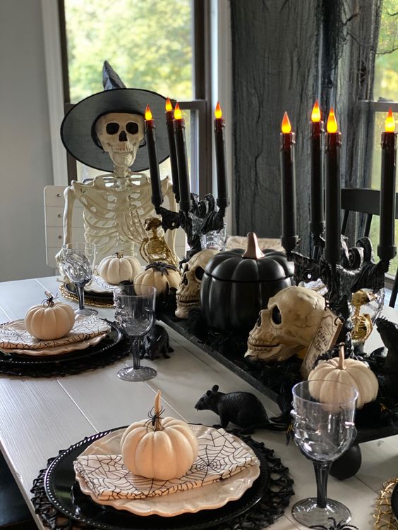 a Halloween centerpiece of black and white skulls, black candelabras with black candles and pumpkins