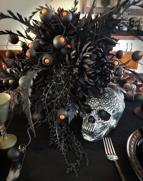 a Halloween centerpiece of black blooms and grasses and leaves, an embellished skull