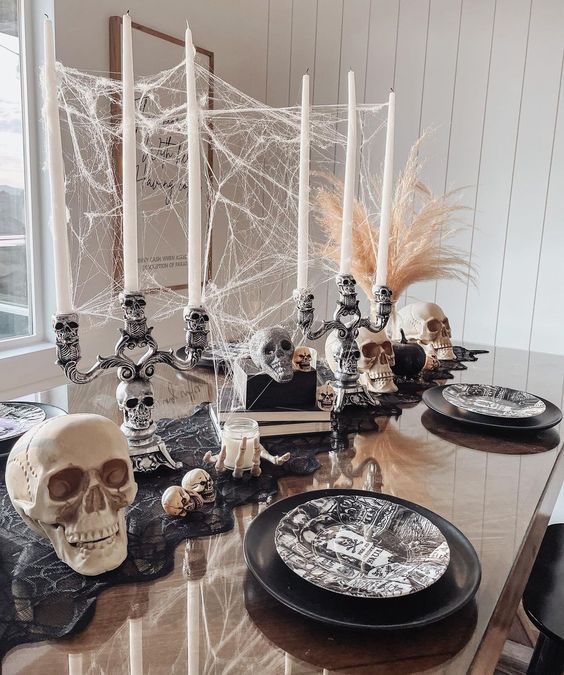 a Halloween centerpiece of skull candelabras with candles, spiderweb, skulls and books is a cool idea