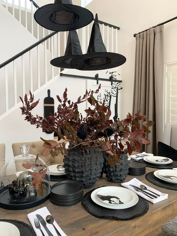 a Halloween centerpiece of two black vases and dark leaves plus witches hats over the table