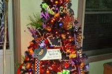 a Halloween tree imitating a witch in a hat, boots and with a broom, with lights, ornaments and hats and letters for fun