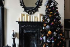 a black Halloween tree decorated with orange and purple ornaments, skulls, spiderwebs and a little house on top