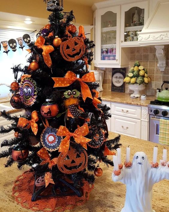 a black Halloween tree decorated with orange bows, cardboard pumpkins, spiderwebs and ornaments as a tabletop decoration