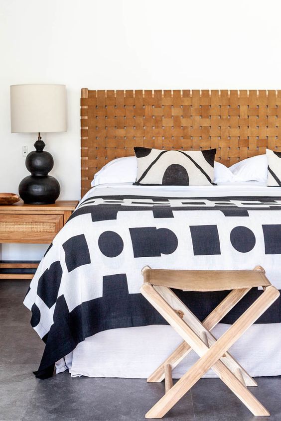 a black and white bedroom with an amber leather woven headboard, black and white bedding, leather stools and stained nightstands