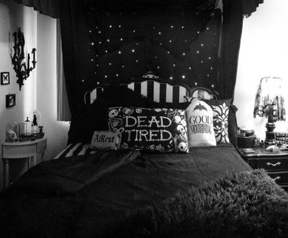 a black and white bedroom with printed pillows, a candelabra on the wall, a lamp and a dark canopy over the bed